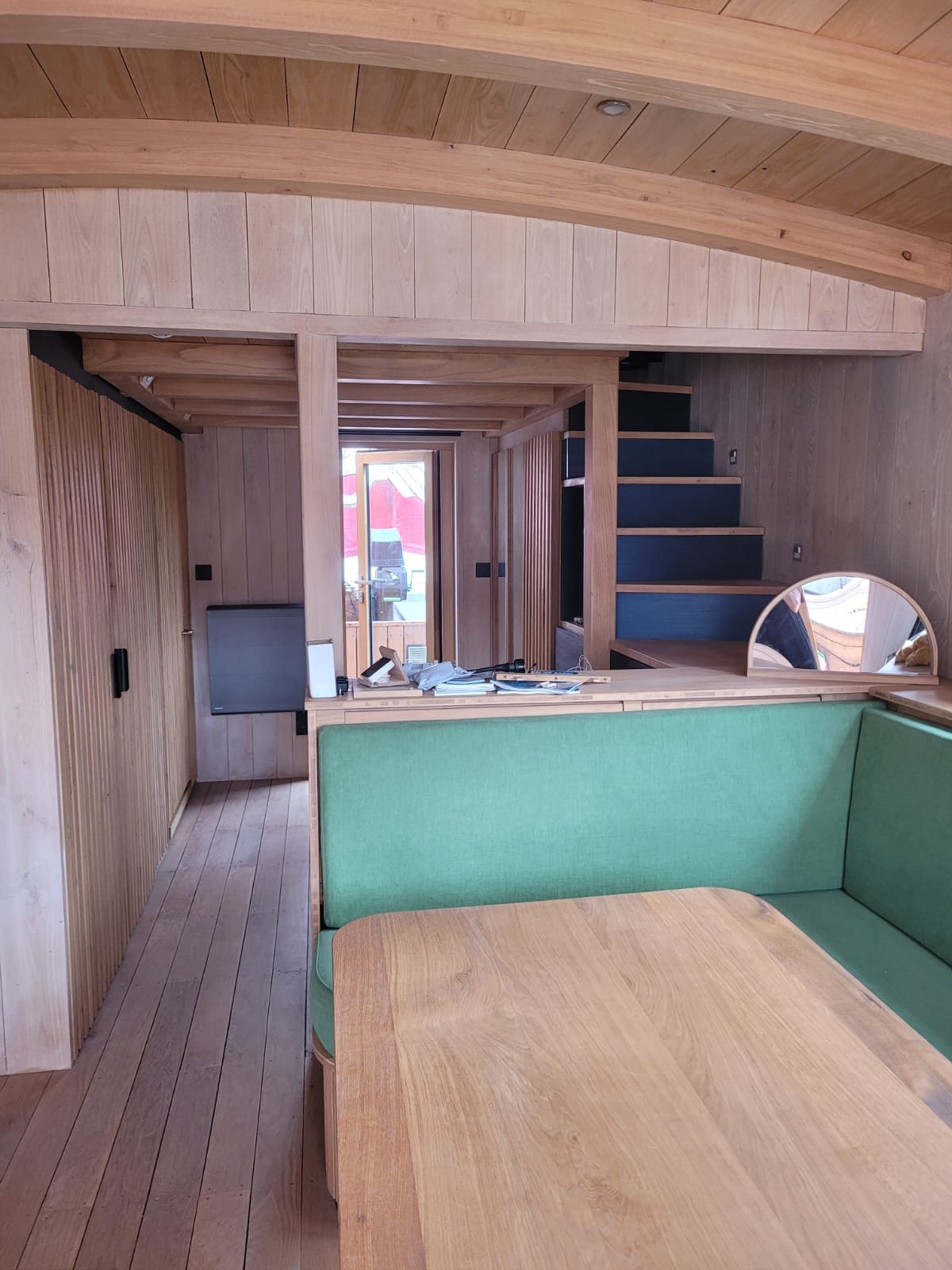 Intérieur du bateau : coque en bois clair, banquette verte et table en chêne